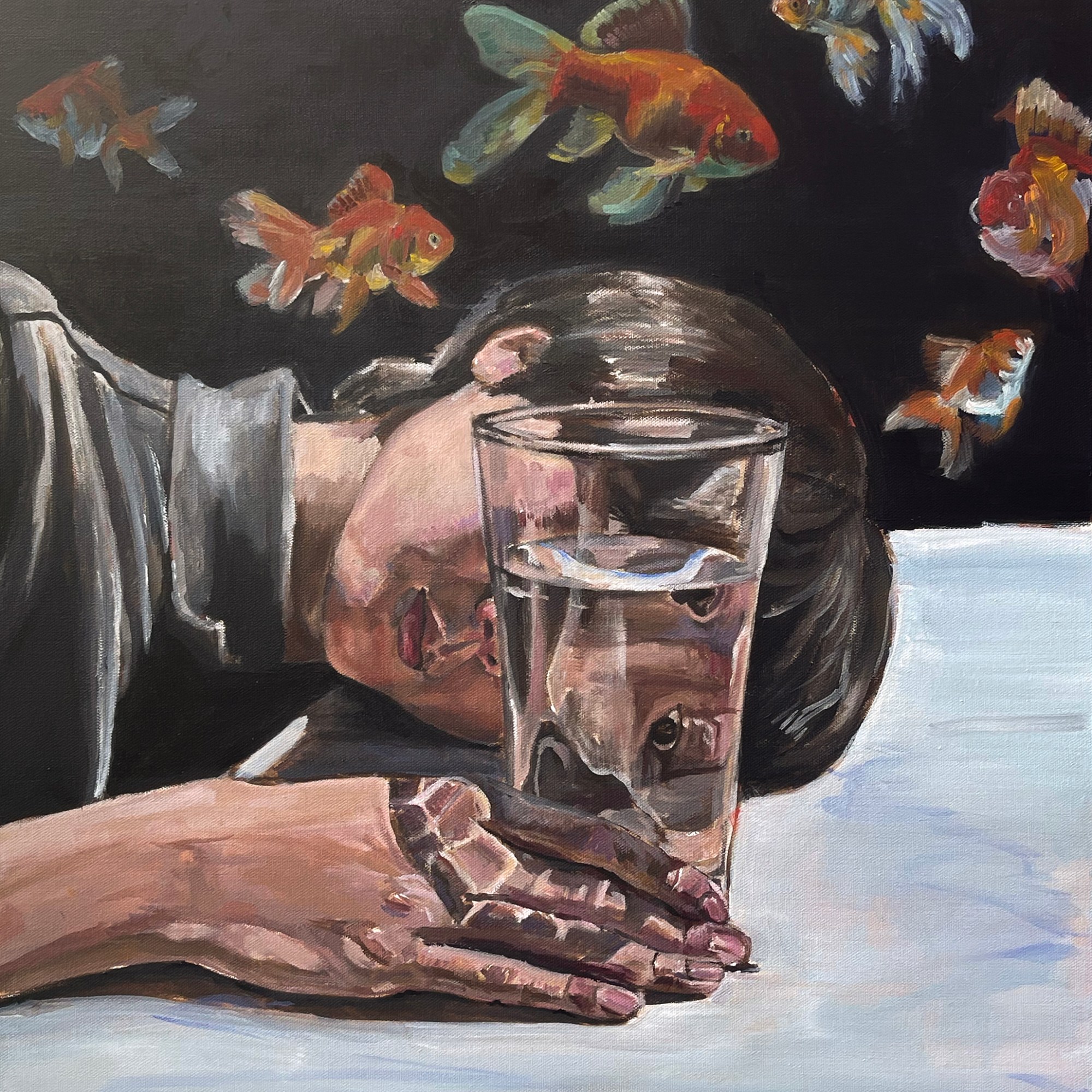 person looking into glass of water with goldfish in background